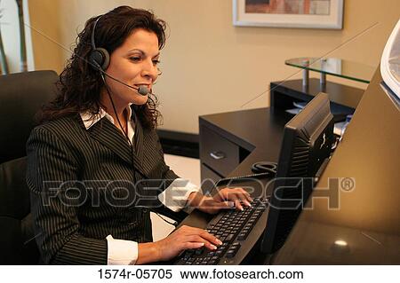 Stock Photography - Side profile of a businesswoman wearing a headset working on a computer. Fotosearch