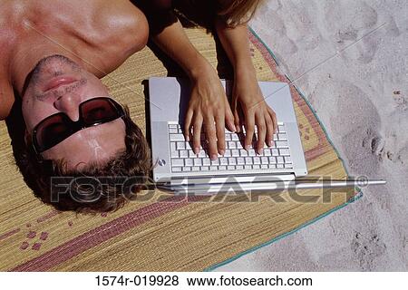 High angle view of a young woman using a laptop with a young man lying beside her View Large Photo Image Stock Photo - High angle view of a young woman using a laptop with a young man lying beside her. Fotosearch