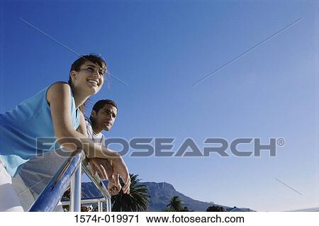 Low angle view of a young couple leaning against a railing View Large Photo Image Stock Image - Low angle view of a young couple leaning against a railing. Fotosearch