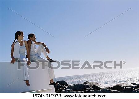 Low angle view of a young couple sitting on a wall near the beach View Large Photo Image Stock Image - Low angle view of a young couple sitting on a wall near the beach. Fotosearch