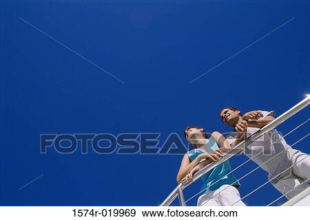 Low angle view of a young couple leaning against a railing View Large Photo Image Stock Photo - Low angle view of a young couple leaning against a railing. Fotosearch