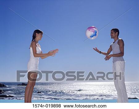 Side profile of a young couple playing with a beach ball View Large Photo Image Stock Photo - Side profile of a young couple playing with a beach ball. Fotosearch