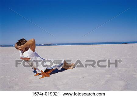 Stock Image - Side profile of a young man sitting on a chair on the beach. Fotosearch
