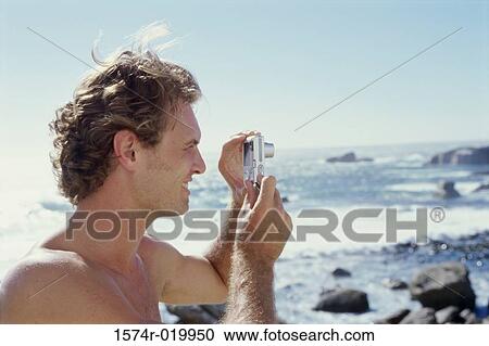 Stock Image - Side profile of a young man taking a photograph with a digital camera. Fotosearch