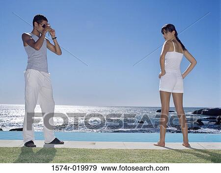 Side profile of a young man taking a photograph of a young woman at the poolside View Large Photo Image Stock Photo - Side profile of a young man taking a photograph of a young woman at the poolside. Fotosearch