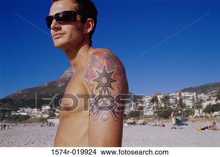 Picture - Side profile of a young man with a tattoo on his arm. Fotosearch