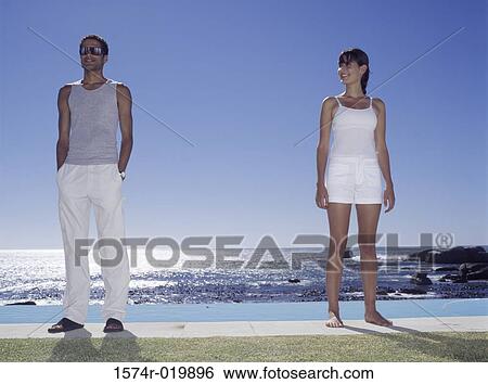 Young couple standing at the poolside View Large Photo Image Stock Photograph - Young couple standing at the poolside. Fotosearch