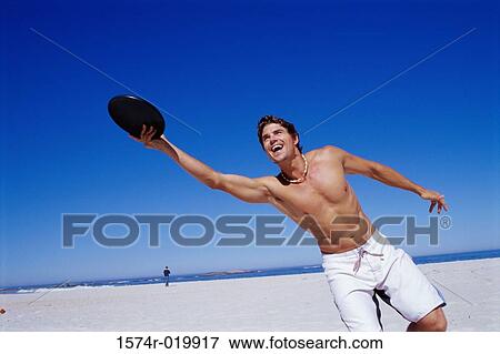 Stock Photo - Young man playing frisbee on the beach. Fotosearch