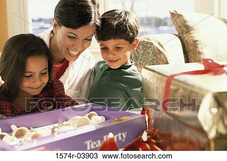 Boy and a girl looking at Christmas present with their mother View Large Photo Image Stock Image - Boy and a girl looking at Christmas present with their mother. Fotosearch