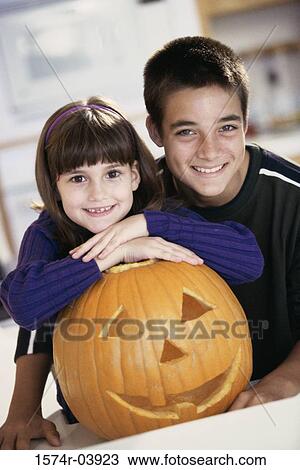 Stock Image - Boy and a girl smiling next to a jack-o-lantern. Fotosearch