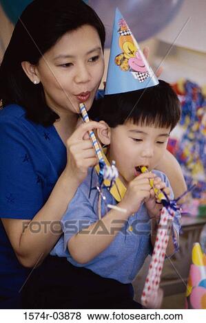 Boy wearing a birthday cap blowing a party horn blower with his mother View Large Photo Image Stock Photo - Boy wearing a birthday cap blowing a party horn blower with his mother. Fotosearch