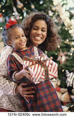 Girl holding a Christmas present and smiling with her mother View Large Photo Image Stock Image - Girl holding a Christmas present and smiling with her mother. Fotosearch