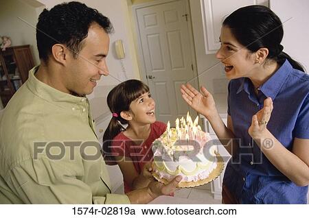 Stock Image - Girl standing in front of a birthday cake with her parents. Fotosearch