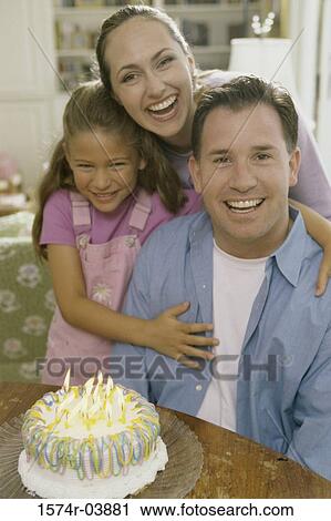 Stock Image - Parents with their daughter in front of a birthday cake. Fotosearch
