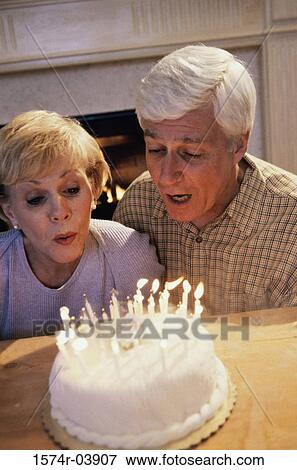 Stock Photo - Senior couple blowing out candles on a cake. Fotosearch