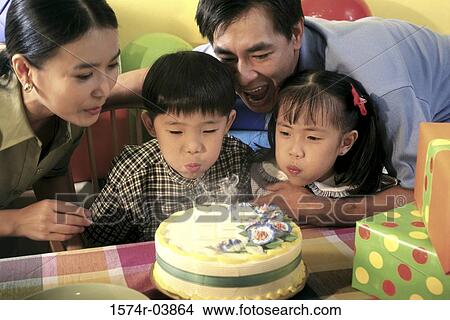 Son and daughter blowing out candles on their birthday cake with their parents behind them View Large Photo Image Picture - Son and daughter blowing out candles on their birthday cake with their parents behind them. Fotosearch