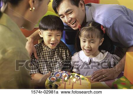 Stock Image - Son and daughter in front of a birthday cake with their parents. Fotosearch