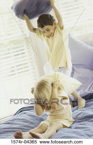 Boy and a girl having a pillow fight on a bed View Large Photo Image Stock Photography - Boy and a girl having a pillow fight on a bed. Fotosearch