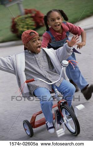 Stock Image - Boy and a girl playing on a tricycle. Fotosearch