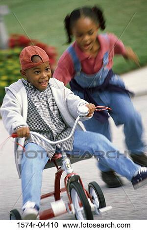 Stock Image - Boy and a girl playing on a tricycle. Fotosearch