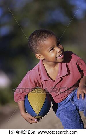 Stock Image - Boy kneeling with a rugby ball. Fotosearch