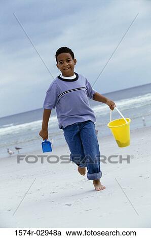 Boy running on the beach carrying a sand pail View Large Photo Image Stock Image - Boy running on the beach carrying a sand pail. Fotosearch