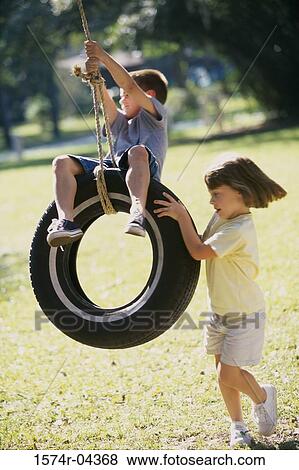 Girl pushing a boy on a tire swing View Large Photo Image Stock Photo - Girl pushing a boy on a tire swing. Fotosearch