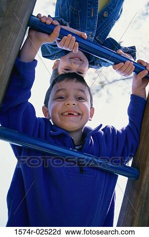 Stock Image - Portrait of a boy and a girl climbing on monkey bars. Fotosearch