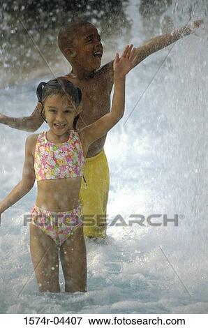 Stock Photo - Portrait of a boy and a girl standing in water on the beach. Fotosearch