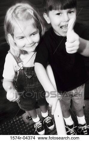 Picture - Portrait of a boy standing with a girl showing thumbs up sign. Fotosearch