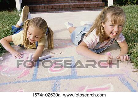 Stock Image - Portrait of two girls drawing on the ground with chalk. Fotosearch