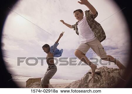 Stock Image - Side profile of two boys jumping on the beach. Fotosearch