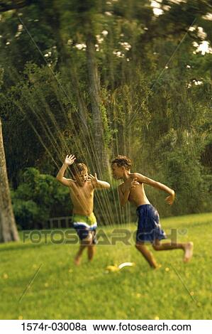 Stock Image - Two boys playing in a water sprinkler. Fotosearch