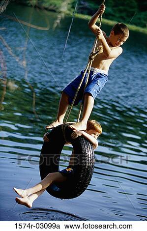 Two boys playing on a tire swing View Large Photo Image Stock Image - Two boys playing on a tire swing. Fotosearch