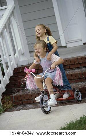 Stock Photo - Two girls playing on a tricycle. Fotosearch