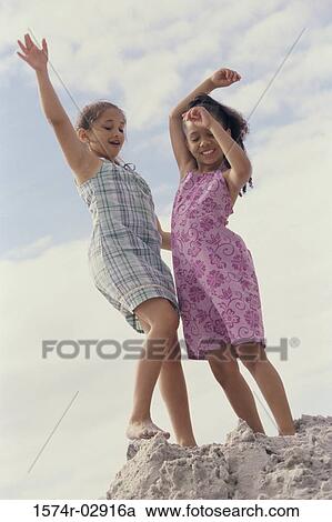 Stock Image - Two girls standing on the beach with their arms raised. Fotosearch