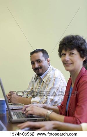 Stock Image - Portrait of a businessman and a businesswoman sitting in a conference room. Fotosearch