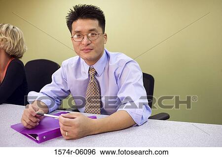 Stock Photograph - Portrait of a businessman and a businesswoman sitting in a conference room. Fotosearch