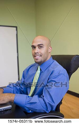 Stock Image - Portrait of a businessman sitting in an office working on a laptop. Fotosearch