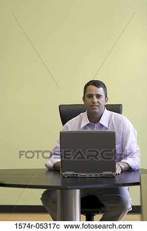 Stock Image - Portrait of a businessman sitting in an office working on a laptop. Fotosearch