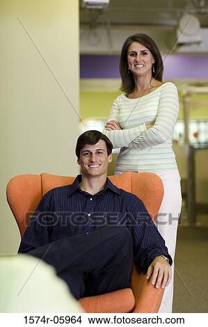 Picture - Portrait of a businessman sitting on a chair with a businesswoman standing behind him. Fotosearch