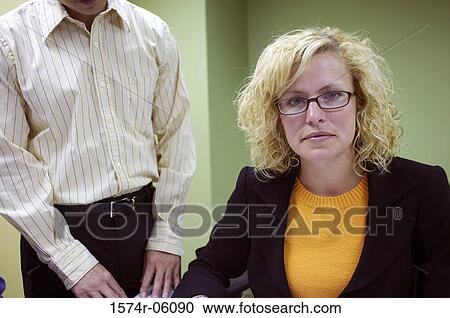 Stock Image - Portrait of a businesswoman sitting in an office with a businessman standing beside her. Fotosearch