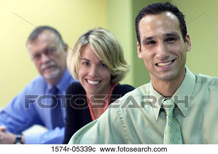 Stock Image - Portrait of two businessmen and a businesswoman sitting in a conference room. Fotosearch