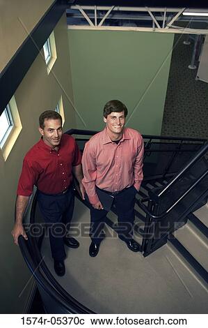 Stock Image - Portrait of two businessmen standing on stairs in an office. Fotosearch