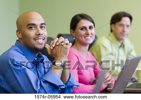 Picture - Two businessmen and a businesswoman sitting in a conference room smiling. Fotosearch