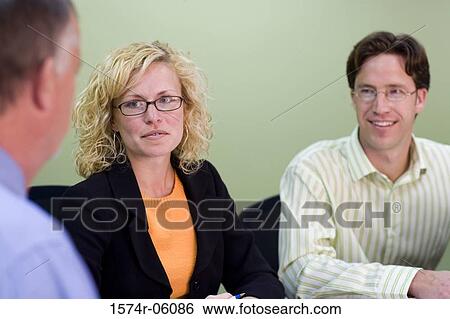 Two businessmen and a businesswoman sitting in a conference room View Large Photo Image Stock Photograph - Two businessmen and a businesswoman sitting in a conference room. Fotosearch