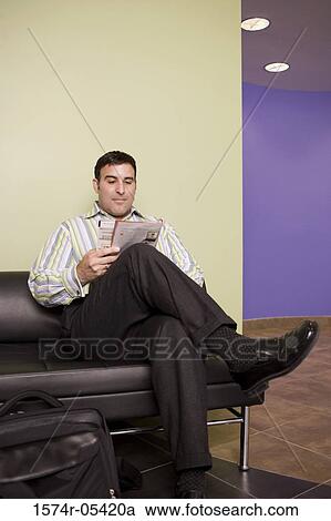 Businessman sitting on a couch reading a magazine View Large Photo Image Stock Image - Businessman sitting on a couch reading a magazine. Fotosearch