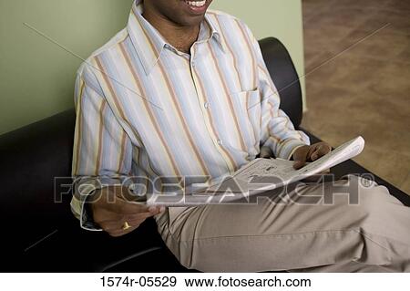 Stock Photo - Close-up of a businessman sitting on a couch reading a newspaper. Fotosearch