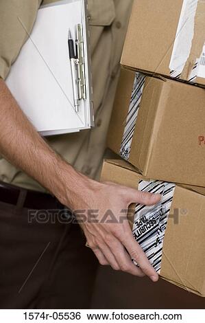 Close-up of a delivery man holding a stack of boxes and a clipboard View Large Photo Image Stock Photograph - Close-up of a delivery man holding a stack of boxes and a clipboard. Fotosearch