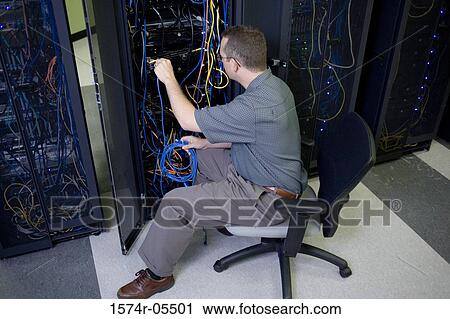 Stock Image - High angle view of a technician attaching cables to a network server. Fotosearch